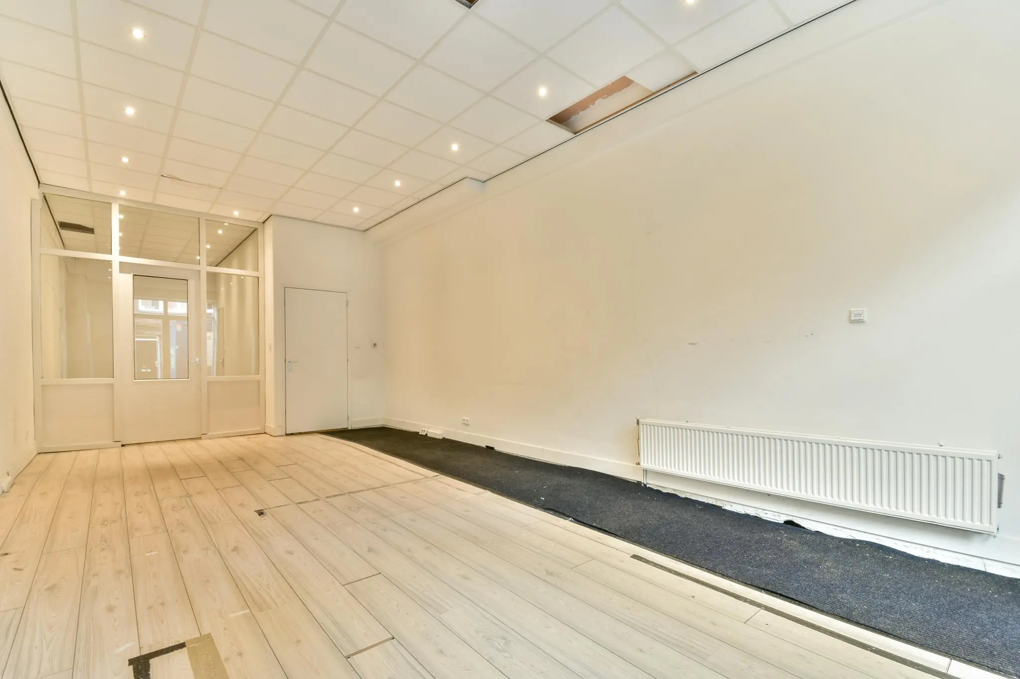 Leegstaand winkelpand aan de Korte Schimmelstraat met houten vloer, systeemplafond en radiator.